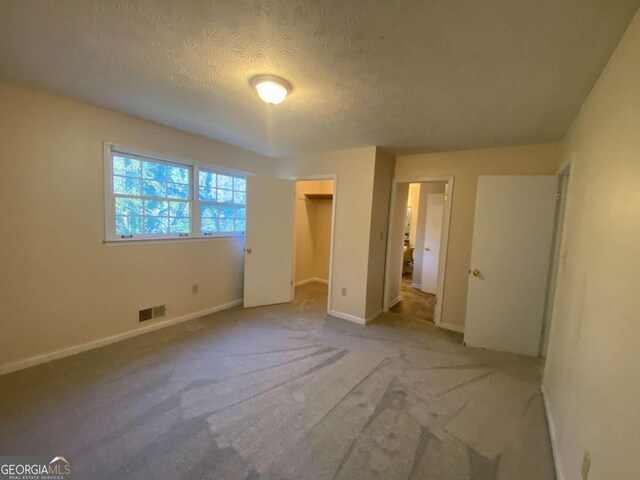 unfurnished bedroom featuring light colored carpet, a spacious closet, a textured ceiling, and a closet