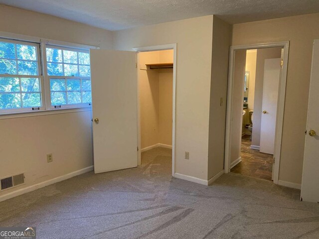 unfurnished bedroom with carpet, a spacious closet, a textured ceiling, and a closet