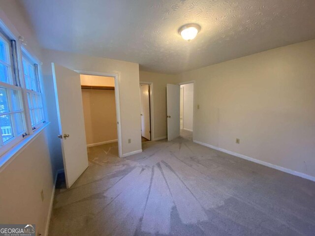 unfurnished bedroom with a walk in closet, light carpet, a closet, and a textured ceiling