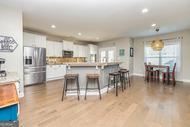 kitchen featuring light stone countertops, stainless steel appliances, light hardwood / wood-style flooring, white cabinets, and a breakfast bar area