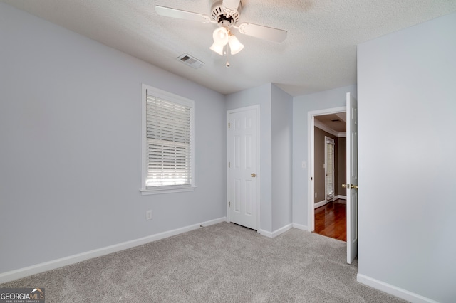 unfurnished bedroom featuring light carpet, a textured ceiling, and ceiling fan