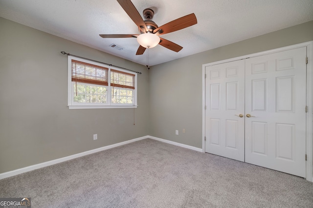 unfurnished bedroom featuring ceiling fan, a closet, light carpet, and a textured ceiling