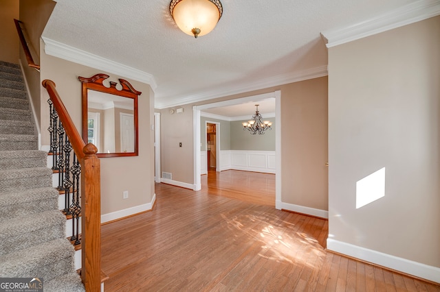 foyer entrance featuring a textured ceiling, wood-type flooring, crown molding, and a chandelier