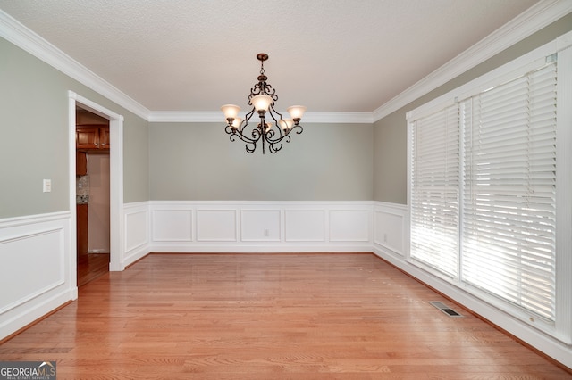 empty room featuring light hardwood / wood-style floors, ornamental molding, a textured ceiling, and a chandelier