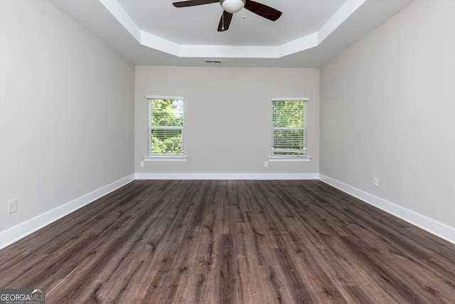 unfurnished room with a raised ceiling, ceiling fan, and dark hardwood / wood-style flooring