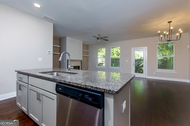 kitchen featuring dishwasher, dark wood-type flooring, sink, light stone countertops, and an island with sink