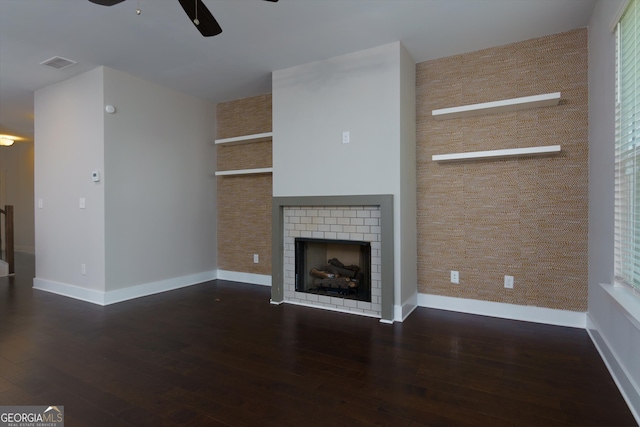 unfurnished living room with ceiling fan, a fireplace, and dark wood-type flooring