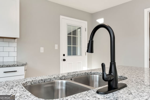 details with sink, light stone counters, white cabinetry, and backsplash