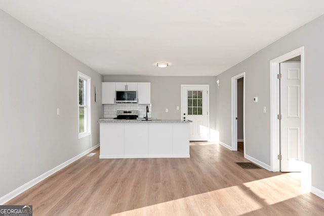 kitchen featuring white cabinets, light wood-type flooring, light stone countertops, tasteful backsplash, and stainless steel appliances