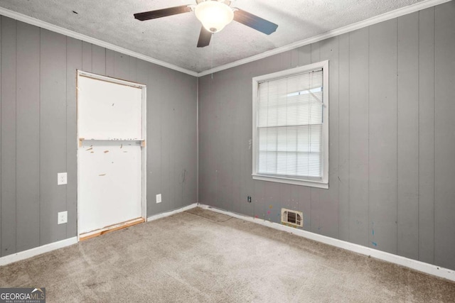 carpeted spare room featuring wooden walls, a textured ceiling, and ornamental molding