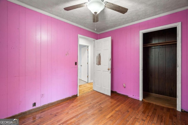 unfurnished bedroom with hardwood / wood-style floors, ceiling fan, crown molding, and a closet