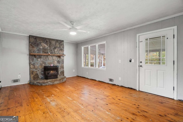 unfurnished living room with hardwood / wood-style flooring, a wood stove, a healthy amount of sunlight, and crown molding