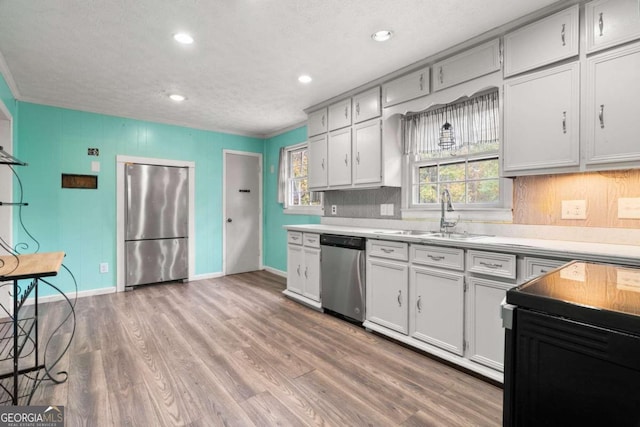 kitchen with sink, light hardwood / wood-style floors, a textured ceiling, white cabinets, and appliances with stainless steel finishes