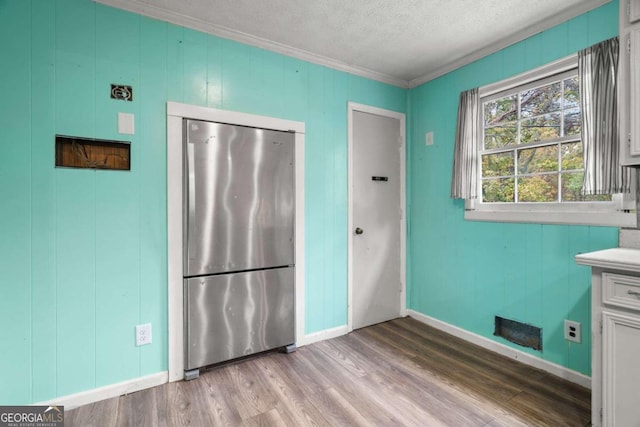 kitchen with ornamental molding, a textured ceiling, white cabinetry, light hardwood / wood-style flooring, and stainless steel refrigerator