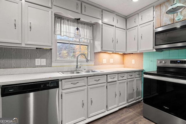 kitchen with appliances with stainless steel finishes, sink, pendant lighting, white cabinets, and dark hardwood / wood-style floors