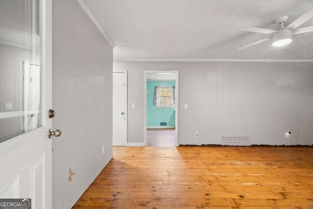 unfurnished room with ceiling fan, light hardwood / wood-style flooring, wood walls, and ornamental molding