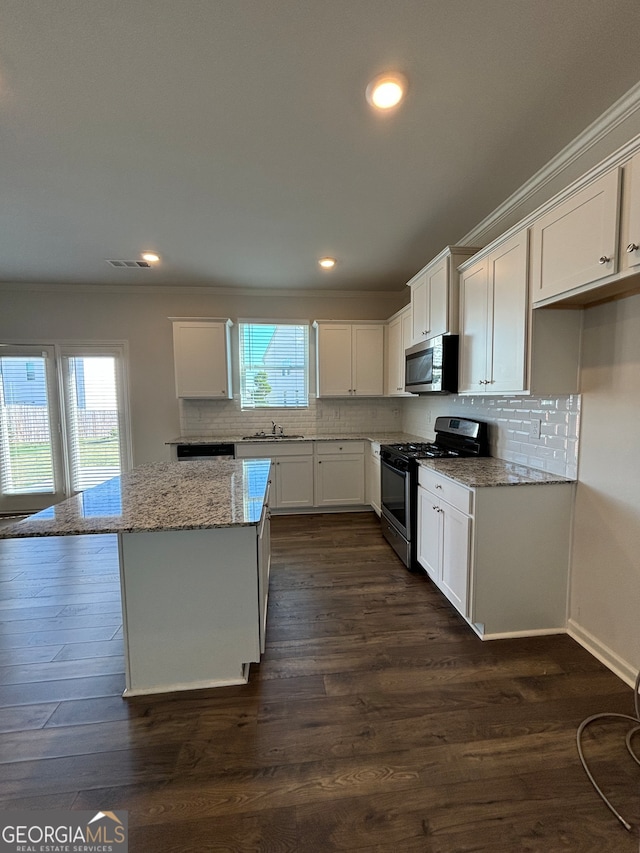 kitchen with light stone countertops, dark hardwood / wood-style flooring, stainless steel appliances, white cabinetry, and a kitchen island