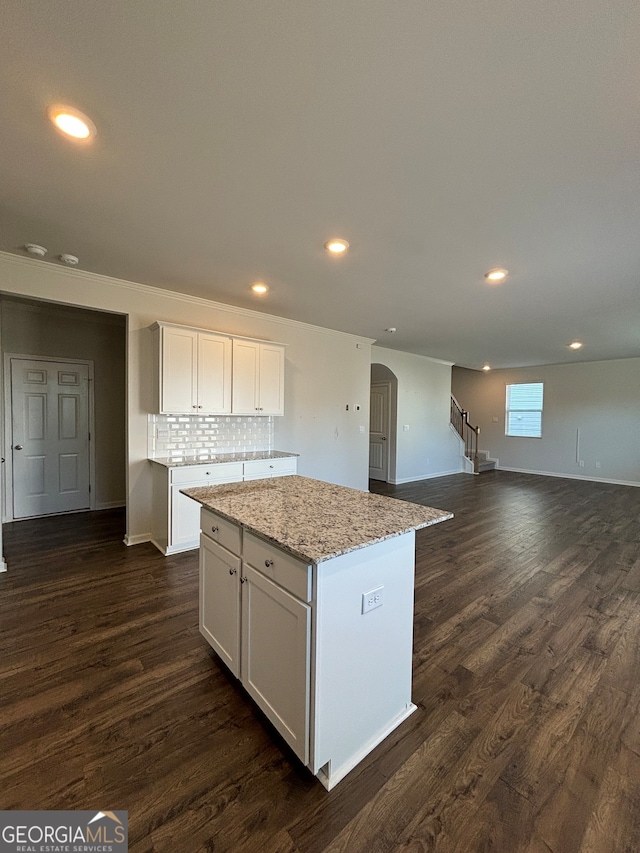 kitchen with white cabinetry, dark hardwood / wood-style flooring, a kitchen island, and light stone countertops