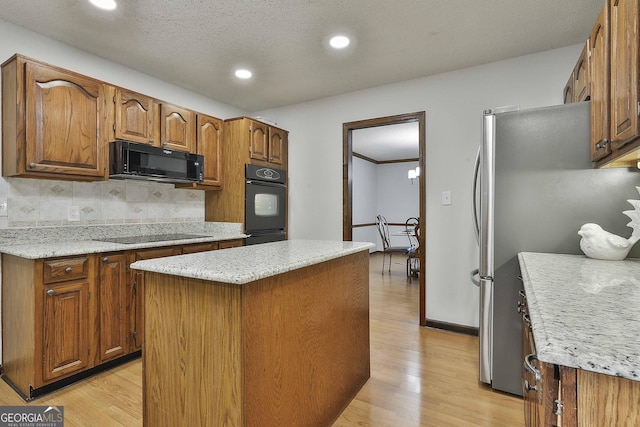 kitchen with light wood-type flooring, backsplash, a kitchen island, and black appliances