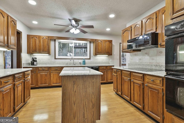 kitchen featuring light wood-type flooring, a textured ceiling, a kitchen island, and black appliances