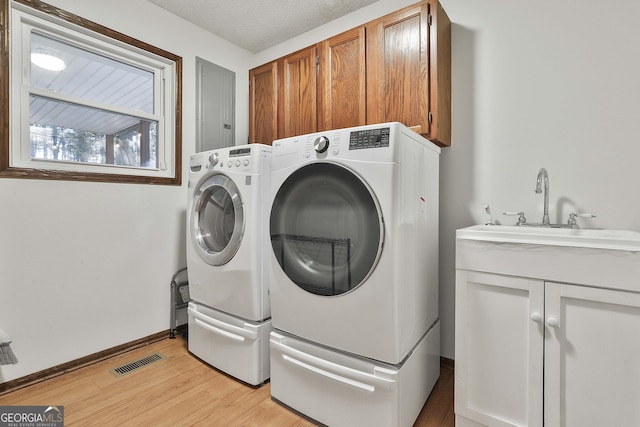 clothes washing area featuring washing machine and clothes dryer, sink, cabinets, light hardwood / wood-style flooring, and a textured ceiling