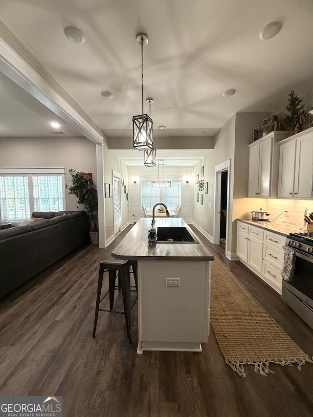 kitchen with white cabinetry, sink, stainless steel gas range oven, an island with sink, and a kitchen bar