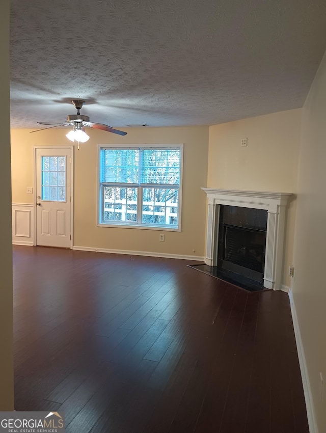 unfurnished living room featuring a tile fireplace, dark wood-type flooring, a wealth of natural light, and a textured ceiling