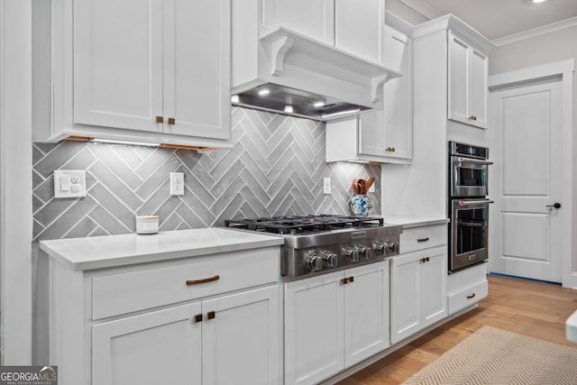 kitchen with backsplash, custom range hood, stainless steel appliances, light hardwood / wood-style floors, and white cabinetry