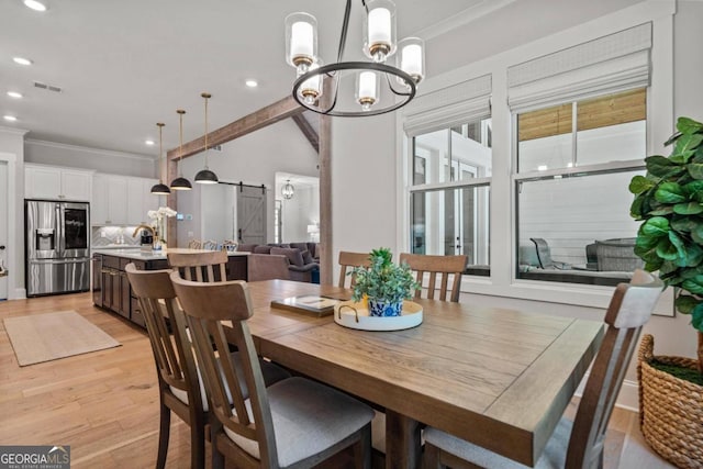 dining area featuring a barn door, sink, light wood-type flooring, and ornamental molding