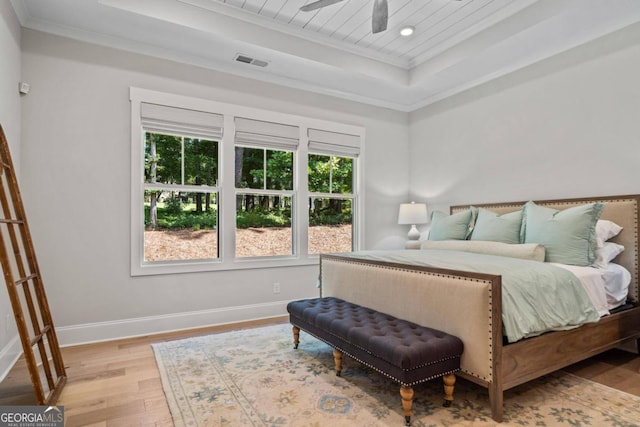 bedroom featuring light wood-type flooring, a tray ceiling, ceiling fan, and crown molding