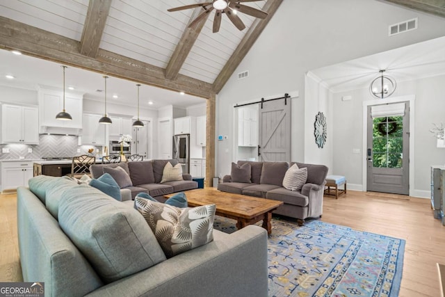 living room with high vaulted ceiling, ceiling fan with notable chandelier, a barn door, light wood-type flooring, and beam ceiling