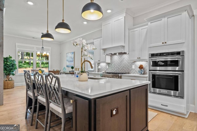 kitchen featuring white cabinets, pendant lighting, light wood-type flooring, and stainless steel appliances