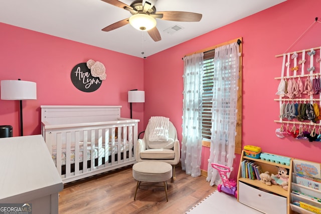 bedroom with a crib, hardwood / wood-style flooring, and ceiling fan