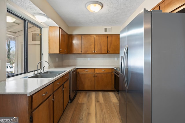 kitchen featuring appliances with stainless steel finishes, sink, light hardwood / wood-style floors, kitchen peninsula, and a textured ceiling