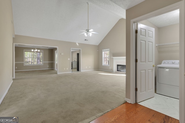 unfurnished living room featuring light wood-type flooring, a textured ceiling, ceiling fan with notable chandelier, vaulted ceiling, and washer / dryer