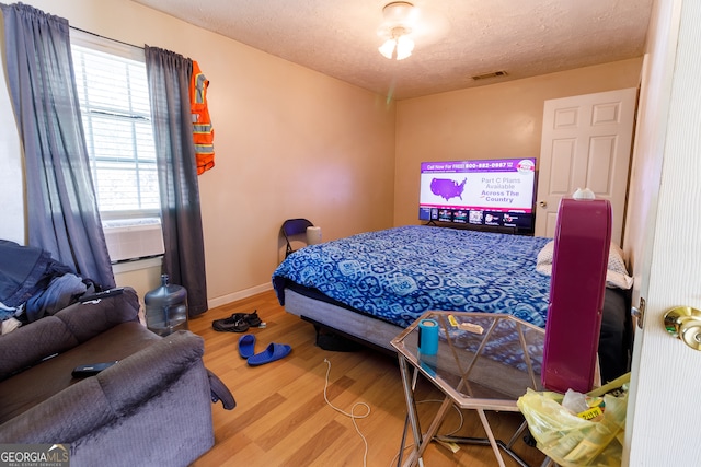 bedroom featuring cooling unit, a textured ceiling, and hardwood / wood-style flooring