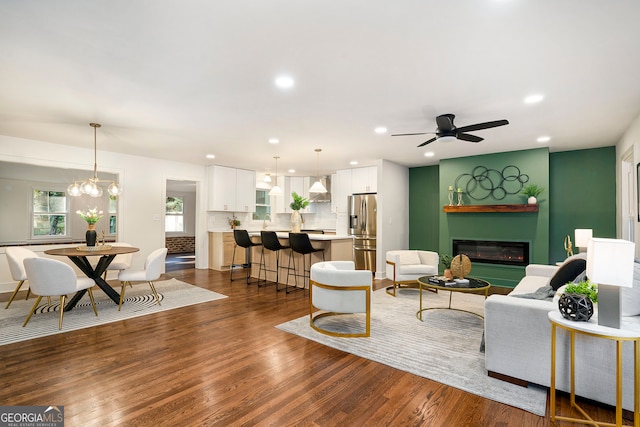 living room with ceiling fan with notable chandelier and dark wood-type flooring