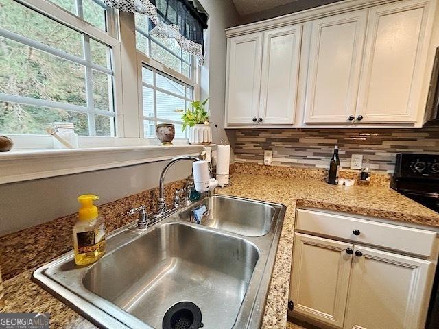 interior details featuring light stone counters, stove, a sink, and decorative backsplash