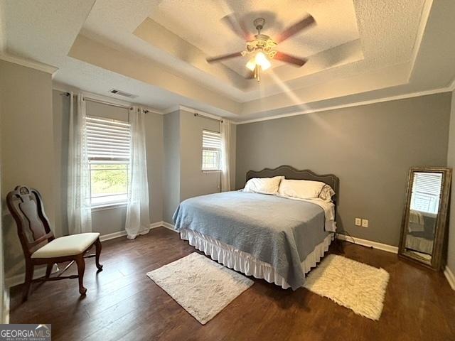 bedroom featuring a raised ceiling, ceiling fan, dark wood-type flooring, and ornamental molding