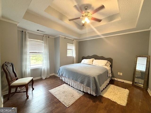 bedroom featuring a raised ceiling, visible vents, a ceiling fan, wood finished floors, and baseboards