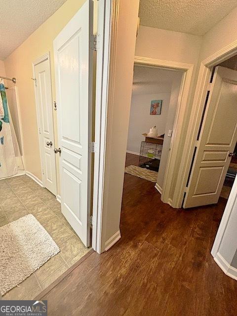 hall with a textured ceiling, baseboards, and wood finished floors