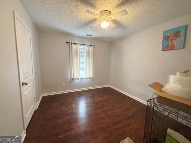 unfurnished room featuring ceiling fan, a textured ceiling, wood finished floors, visible vents, and baseboards