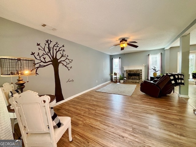 living room with a textured ceiling, hardwood / wood-style flooring, a stone fireplace, and ceiling fan