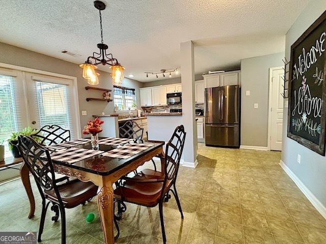 dining area featuring baseboards, track lighting, visible vents, and a textured ceiling