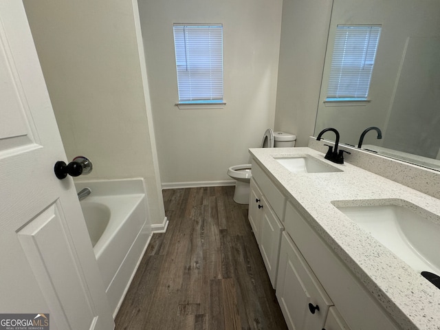 bathroom with hardwood / wood-style flooring, vanity, toilet, and a tub to relax in