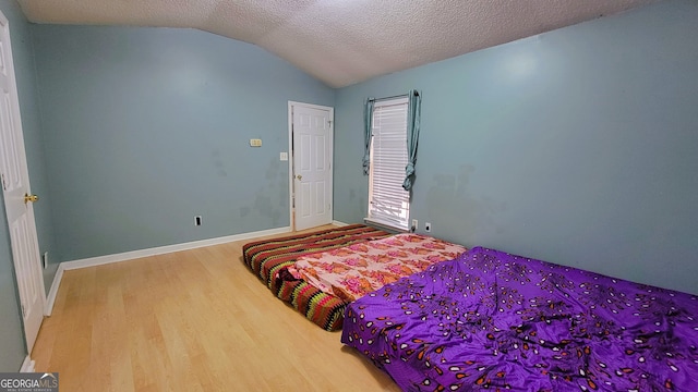 bedroom featuring vaulted ceiling, wood-type flooring, and a textured ceiling