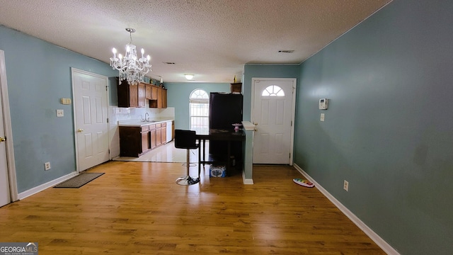 entryway featuring a textured ceiling, light wood-type flooring, an inviting chandelier, and sink