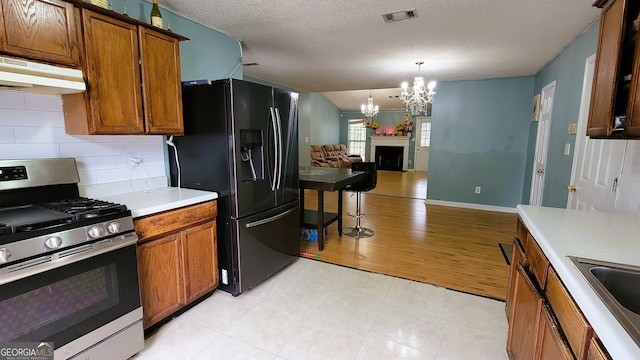 kitchen with decorative backsplash, black fridge, a textured ceiling, gas stove, and a notable chandelier