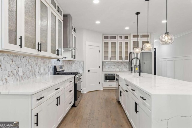 kitchen with pendant lighting, white cabinets, light wood-type flooring, light stone counters, and stainless steel appliances