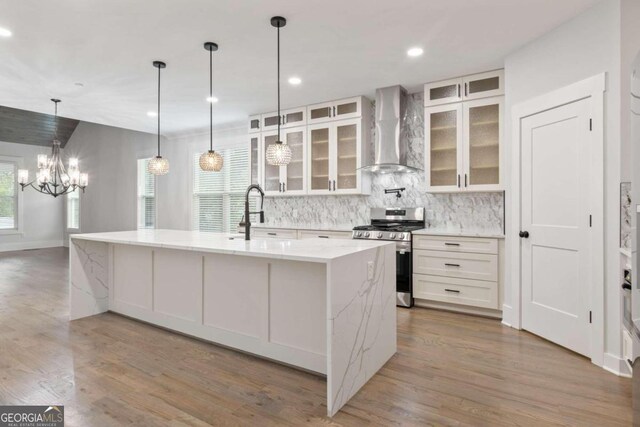 kitchen featuring a kitchen island with sink, sink, stainless steel stove, wall chimney exhaust hood, and light wood-type flooring